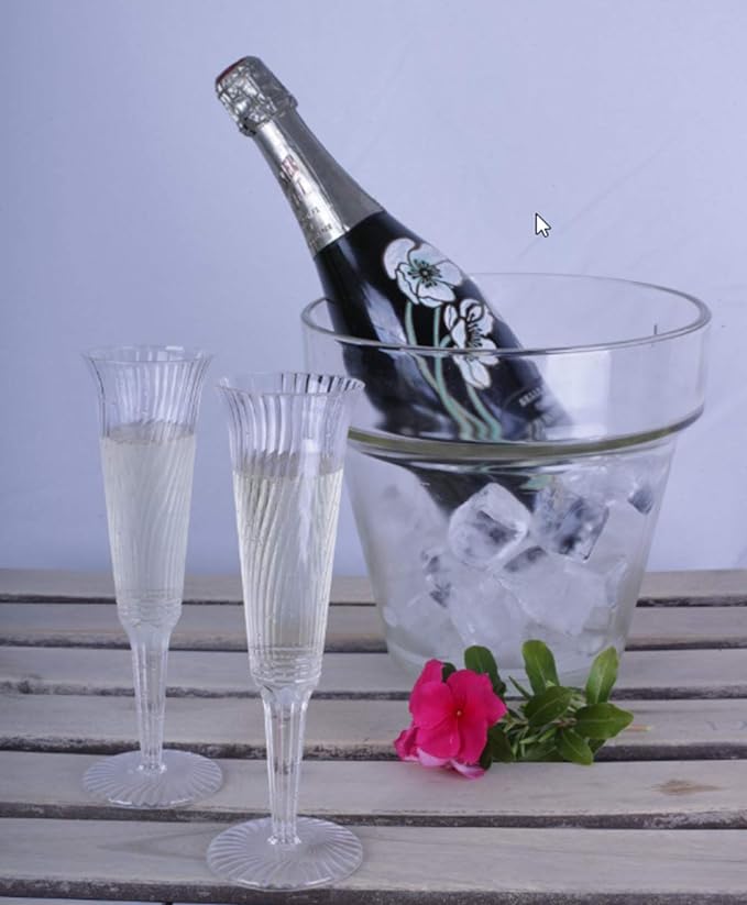 A set of two champagne glasses next to a bottle of champagne on ice.  These plastic champagne flutes are available in bulk for parties and events.