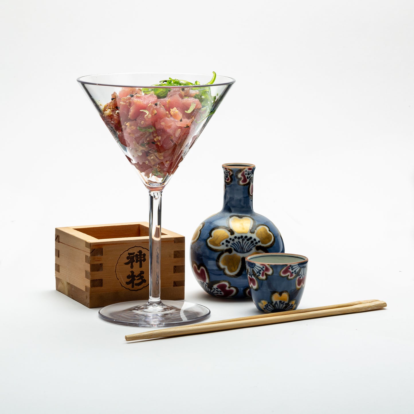 A disposable and reusable martini glass used as a dish to hold poki with Asian influenced decor around the plastic martini glass